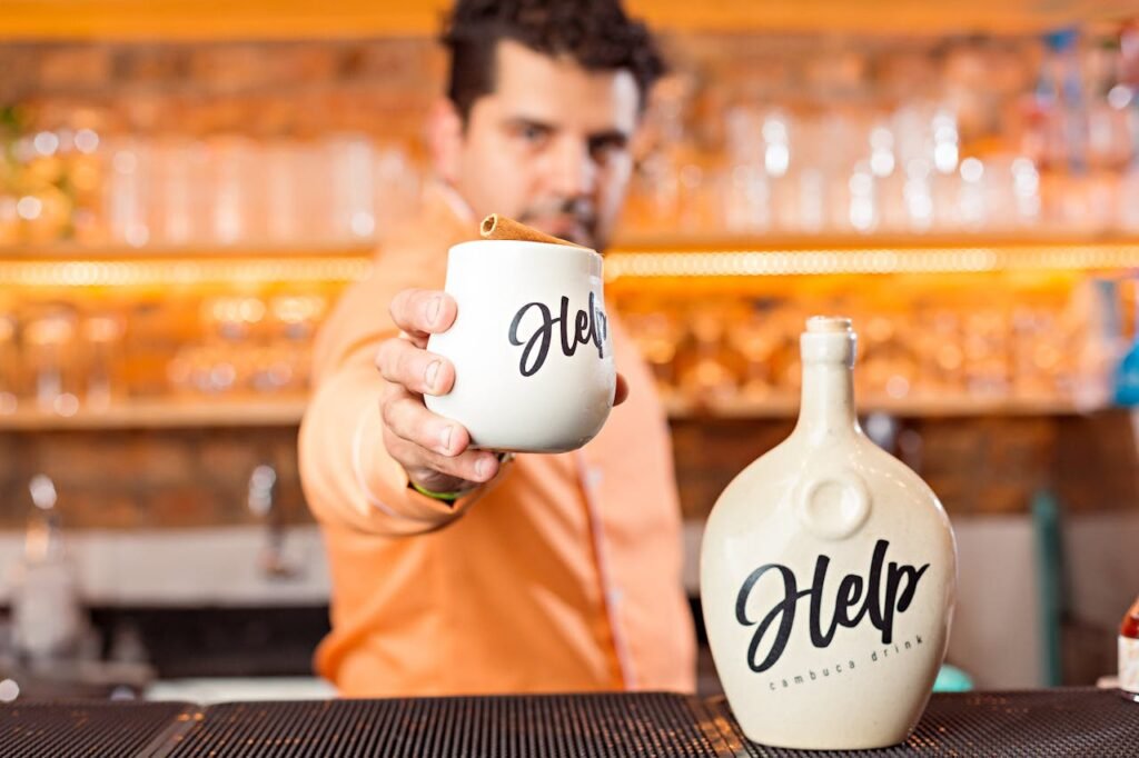 pexels-photo-14161907 A bartender offers a ceramic mug with 'Help' branding in a modern bar setting, highlighting drink service.